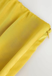 Tissu jaune vif avec un détail élastique froncé et une fermeture éclair jaune fermée sur un fond blanc.