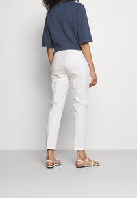 Lätta vita byxor med skräddarsydd passform, raka ben och subtila bakfickor. Dessa är kombinerade med en mörkblå kortärmad topp och vita sandaler.