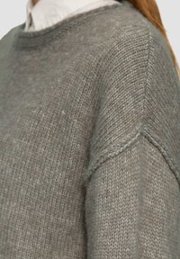 Jasnoszara dziana sweter z okrągłym dekoltem, luźnym krojem oraz teksturowanym materiałem z widocznymi szwami i szwami na ramionach.