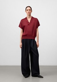 Top corto in satin borgogna a maniche corte con scollatura a V, abbinato a pantaloni neri a gamba larga con vita alta. Tessuto morbido, vestibilità comoda.