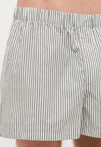 Shorts rayés avec une coupe décontractée, présentant des rayures verticales grises et blanches fines alternées, une taille élastique et une texture en coton douce.