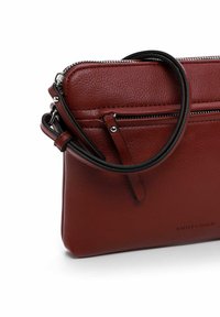 Bolso bandolera de cuero rojo con superficie texturizada, que cuenta con un bolsillo con cremallera, una correa negra y detalles de hardware plateados.