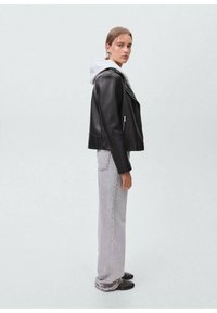 Giubbotto di pelle nera con zip argentate, indossato sopra un felpa grigia con cappuccio. Abbinato a jeans dritti grigio chiaro e scarpe slip-on nere.