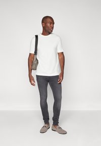 Witte katoenen T-shirt, slim-fit donkergrijze spijkerbroek, grijze crossbody tas met strap en grijze suède schoenen. Eenvoudig ontwerp en casual uitstraling.