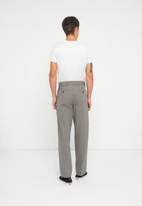 Gray checkered trousers with a loose fit, featuring standard pockets and a waistband. Paired with a plain white t-shirt and black shoes.