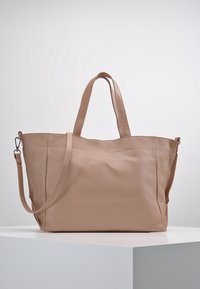 Beige läder tote-väska med två topphandtag och en avtagbar axelrem, visad på en vit pedestal mot en enkel bakgrund.