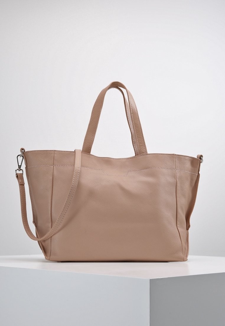 Beige läder tote-väska med två topphandtag och en avtagbar axelrem, visad på en vit pedestal mot en enkel bakgrund.