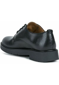 Scarpa oxford in pelle nera, con punta tonda, suola piatta e cuciture decorative. L'interno è in pelle beige con un collare imbottito.