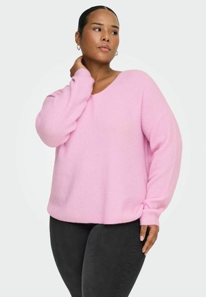 Rosa strikkegenser med V-hals, løse ermer og ribbestruktur. Brukt med mørkegrå bukser, vist mot en lys bakgrunn.