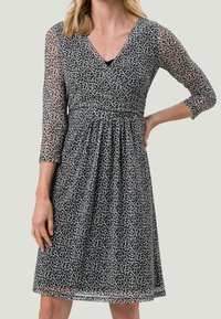 Vestido blanco y negro con un patrón de hojas, escote en v, mangas tres cuartos de tejido transparente, cintura ceñida y falda fluida.
