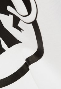 Biała tkanina o gładkiej strukturze z wyraźnym czarnym wzorem graficznym, zawierającym krzywe kształty i ostre krawędzie.