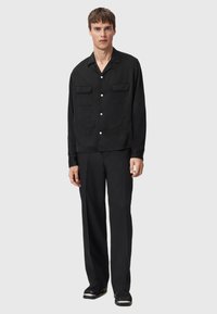 Czarna koszula z krótkim rękawem, zapinana na guziki, z dwiema kieszeniami na piersiach i haftowanymi detalami, zestawiona z dopasowanymi czarnymi spodniami i czarnymi butami.