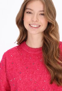 Rózsaszín pulóver texturált felülettel, több színű gyöngy díszítéssel az elején. Bordás nyak és puha anyag.