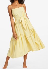 Gelbes ärmelloses Maxikleid mit quadratischem Ausschnitt, anliegendem Oberteil und gebundenem Gürtel. Es verfügt über einen gestuften Rock aus weichem, fließendem Stoff.