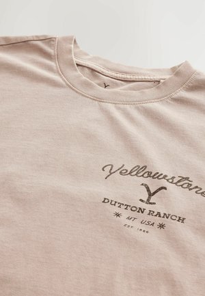 Helles rosa Baumwoll-T-Shirt mit Rundhalsausschnitt. Mit schwarzem Grafiktext "Yellowstone Dutton Ranch MT USA" und dem Gründungsdatum.