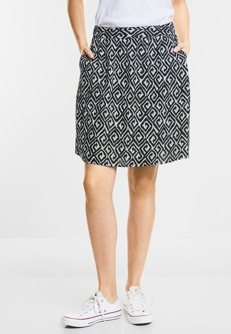 Černá a bílá sukně se geometrickým vzorem, s pasem a bočními kapsami, nošená s bílými teniskami.