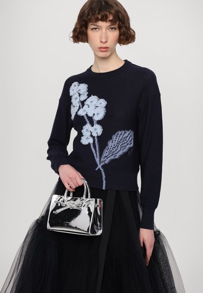 Navy knit sweater with light blue floral embroidery, paired with a black tulle skirt and a transparent handbag featuring a bow detail.