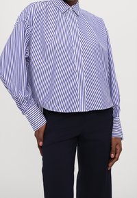 Blå och vit randig skjorta med knappar, krage, oversize passform och långa ärmar; strukturerade manschetter med en liten knappdetalj.