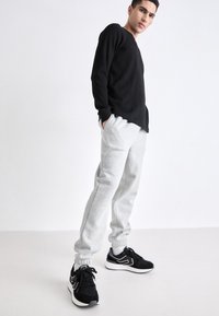 Zwarte lange mouwen shirt met een gestructureerde stof, gecombineerd met grijze sweatpants met elastische boorden. Zwarte sportieve schoenen met witte accenten.