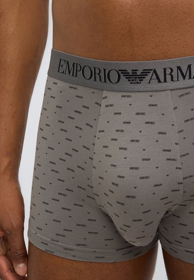 Graue Boxershorts mit wiederholtem schwarzem "Armani"-Textmuster, ausgestattet mit einem breiten grauen Bund mit "Emporio"-Logo in Schwarz, aus weichem Stoff gefertigt.