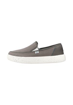Zapato gris tipo slip-on con suela de goma blanca con motas y pequeña etiqueta de tela en el lateral sobre fondo blanco.