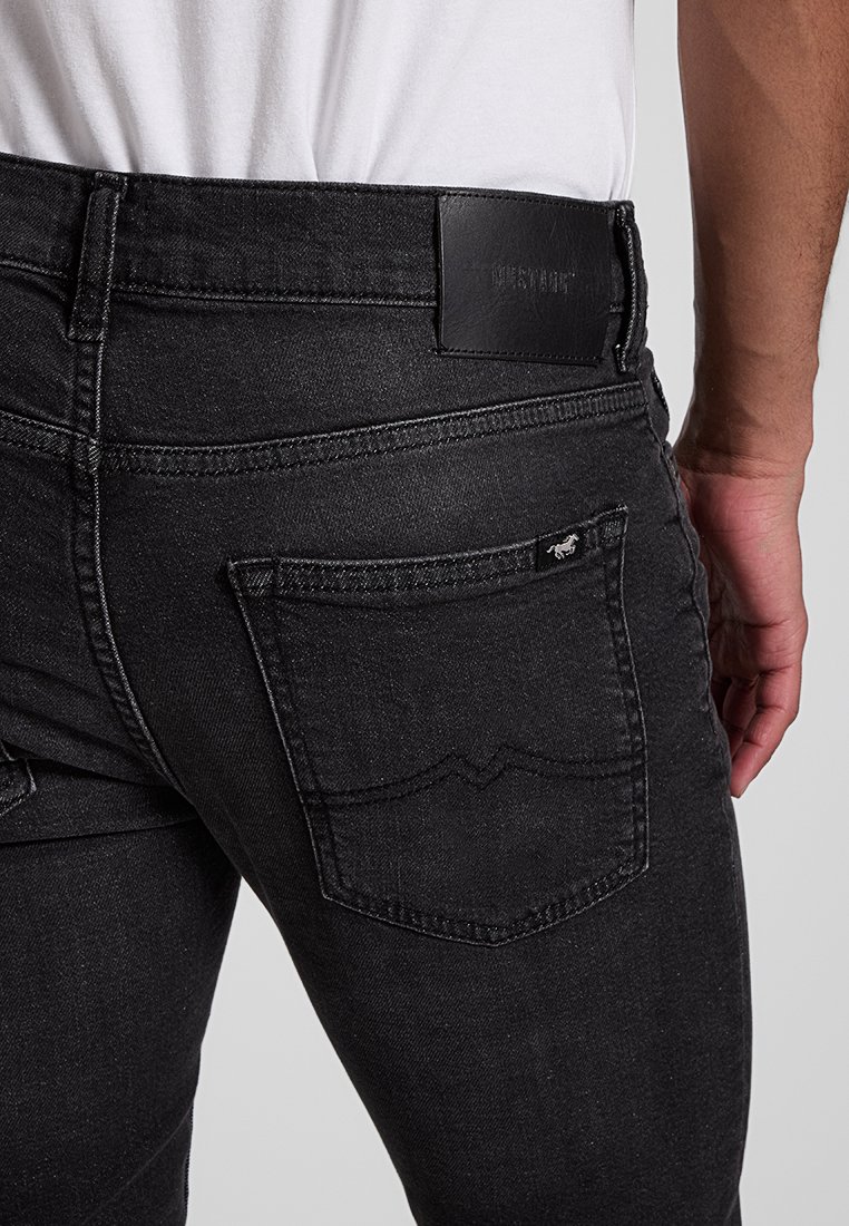 Czarne dżinsy o slim fit, z widocznymi tylnymi kieszeniami i skórzaną naszywką przy pasku. Posiadają subtelne detale w szyciu oraz ciemne wykrojenie.