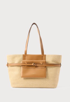 Grand sac fourre-tout tissé beige avec deux poignées en cuir marron, une pochette avant en cuir et une sangle horizontale en cuir avec un détail en nœud.