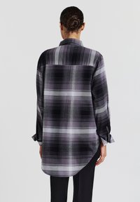 Karierte Hemd mit einer Mischung aus Schwarz, Grau und Lavendel. Verfügt über lange Ärmel, einen abgerundeten Saum und einen Button-Down-Kragen.