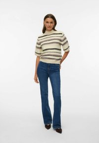 Lühikeste varrukatega kootud kampsun, mis on valmistatud pehmest kreemjas kangast mitmevärviliste triipudega. Sobitatud siniste kitsaste lehvikutega teksade ja teravate jalanõudega.