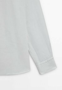 Ljusgrå långärmad skjorta med slät textur, rundad fåll och knäppt ärmslut. Tillverkad av ett lätt och andningsbart material.