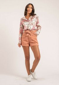 Chemise à manches courtes à fleurs en blanc, rose et vert ; short taille haute pêche avec ceinture et poches ; baskets blanches.