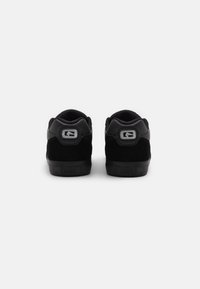 Zapatillas negras de material de gamuza y malla, que cuentan con un collarín acolchado, suela de goma y un acento de logo plateado en el talón.