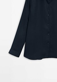 Chemise à manches longues bleu marine, en tissu lisse, avec une fermeture à boutons sur le devant, un col et un ourlet arrondi. Manches à manches retroussées avec des détails de couture soignés.