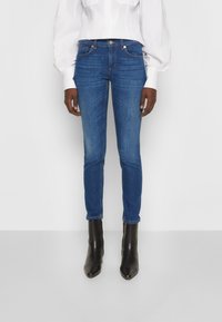 Smala blå jeans med en slät yta, som har fem fickor, bältesöglor och medelhög midja, i kombination med svarta ankelstövlar.