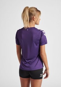 Paarse sportshirt met korte mouwen, voorzien van witte chevronpatronen op de schouders, gemaakt van glad, vochtafvoerend materiaal.