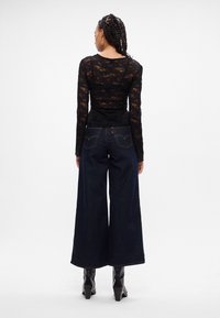 Zwarte kanten top met lange mouwen en een getailleerde taille, gecombineerd met wijde donkerblauwe spijkerbroek met achterzakken en contrasterende stiksels.