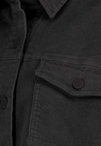 Black corduroy shirt featuring a textured design, button front, and chest pockets with round black buttons.