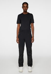 Svart kortärmad skjorta med dragkedja framtill, tillsammans med svarta cargobyxor med dragkedjefickor och en avslappnad passform, matchat med beige sneakers.