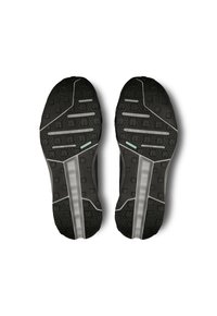 Semelles de chaussures de sport noires en caoutchouc texturé pour l'adhérence, avec un motif géométrique et des accents gris sur les côtés.