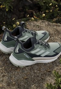 Světle zelené a tmavě modré atletické boty s texturovaným svrškem, bílou mezipodešví a třemi bílými pruhy po straně. Viditelné logo GORE-TEX.