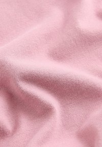 Material de culoare roz deschis, cu o textură moale și netedă și un model de tricotaj fin, evidențiind pliuri și cute delicate.