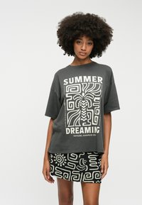 T-shirt gris surdimensionné avec un imprimé graphique blanc portant l'inscription "RÊVES D'ÉTÉ". Associé à une jupe noire à motifs avec des designs abstraits.