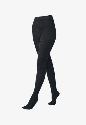 Collants noirs texturés montrés de la taille aux pieds avec les jambes croisées sur fond blanc.