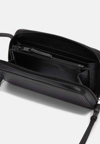 Borsa a tracolla nera in pelle con chiusura a zip. L'interno presenta diversi slot per carte e una tasca con zip, texture liscia, design minimalista.