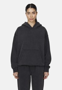 Felpa grigia scura realizzata in tessuto morbido, con un grande tascone frontale, maniche larghe e testo in rilievo sul petto.