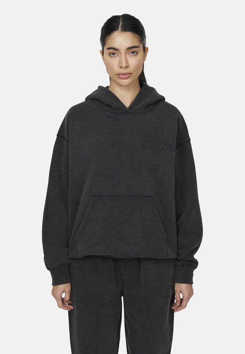 Felpa grigia scura realizzata in tessuto morbido, con un grande tascone frontale, maniche larghe e testo in rilievo sul petto.