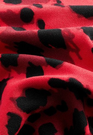 Rode stof met een gestructureerd oppervlak, voorzien van een gedurfde zwarte luipaardprint, die een abstract, organisch ontwerp overbrengt.