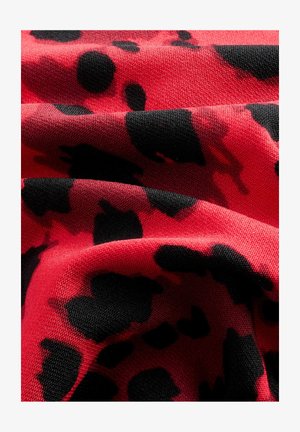 Czerwona tkanina o teksturowej powierzchni, z wyraźnym czarnym wzorem w panterę, przekazująca abstrakcyjny, organiczny design.