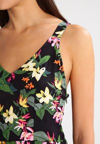 Blumenmuster-Kleid mit leuchtend gelben, rosa und orangen Blumen auf schwarzem Hintergrund. Spaghettiträger und ein V-Ausschnitt.