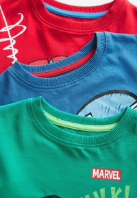 Tre foldede børne Marvel T-shirts i rød, blå og grøn med ribstrikkede runde halsudskæringer og delvise grafiske tryk.